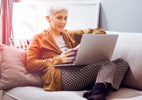 Frau sitze auf dem Sofa mit Laptop und macht Online-Banking